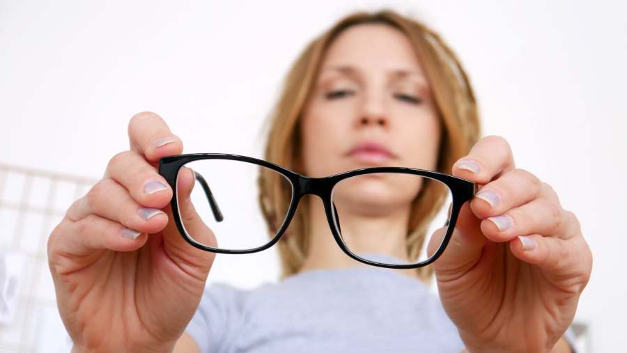 Close-up of black-framed glasses in the hands of a young woman considering her myopia treatment options.