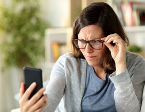 middle-aged woman holding her phone at arm’s length illustrating presbyopia as a cause of blurry vision