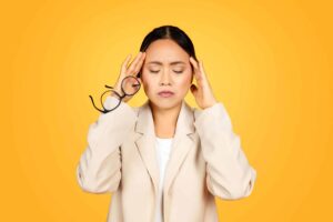 Woman with headache holding glasses showing signs you may need an eye exam